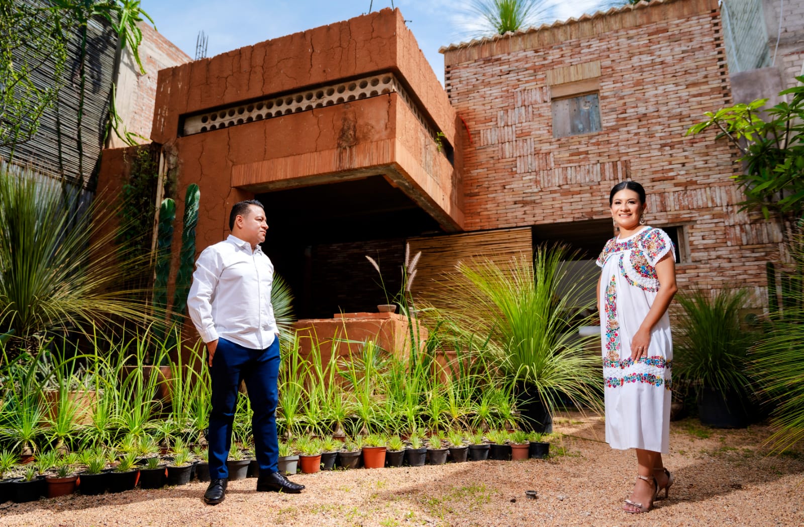 Lili y Luis en el jardín, con la arquitectura de barro de fondo